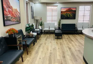 Modern dental office waiting room with seating, plants, artwork, and wood flooring.