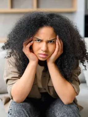 Young woman with curly dark hair resting head on hands, looking thoughtful or concerned indoors.